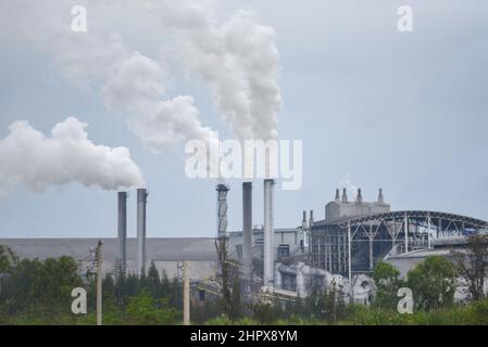 Weißer Rauch kommt aus Rauchgassen oder Abluftrohren in den Fabrikschornsteinen und gibt Wasserdampf ab, der sich vor dem Verdampfen zu einer weißlichen Wolke kondensiert Stockfoto