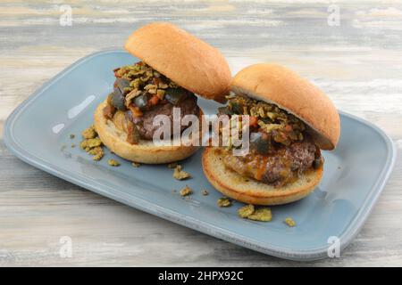Zwei Hamburger mit Käse innen auf Brötchen mit Chili-Belag auf blauem Servierteller Stockfoto