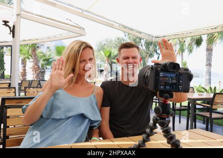Glückliches Paar, das auf einem Stativ in einem Café auf die Kamera winkt Stockfoto