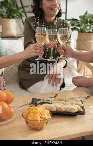 Beschnittenes Bild von älteren Frauen, die Gläser mit Champagner und leckerem Essen zu Hause anklimmten Stockfoto