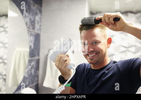 Glücklicher Mann, der zu Hause sein eigenes Föhnen macht Stockfoto