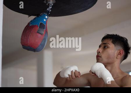 Leichter Boxer trainiert seine Geschwindigkeit und Koordination, indem er den Boxsack mit verbundenen Händen stanzt Stockfoto