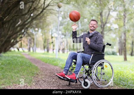 Glücklicher Mann im Rollstuhl dreht den Ball auf seinem Finger im Park Stockfoto