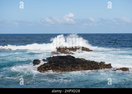 Die Welle trifft am Strand auf den Felsen, das Meerwasser spritzt auf das Meer. Seascape. Spritzer von den Wellen, die gegen das felsige Ufer stoßen. Stockfoto