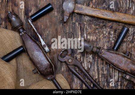 Handwerkzeuge. Zangen, Bohrer, Hammer und raues Stoff-Absacken auf dunklem Holzhintergrund. Rissige Holzoberfläche mit Rissen und Splittern. Selektiver Fokus Stockfoto