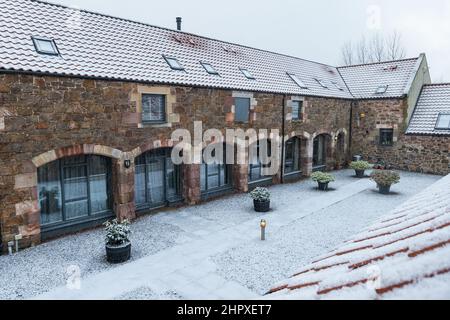 East Lothian, Schottland, Großbritannien, 24.. Februar 2022. UK Wetter: Schnee fällt im Winter auf umgebaute Steadehäuser Stockfoto