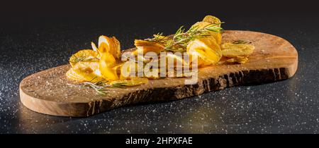 Einige frittierte, spiralförmig geschnittene Kartoffeln mit etwas Thymian auf Holzbrett Stockfoto