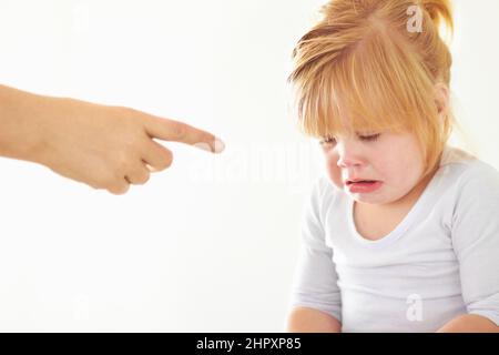 Disziplin - es macht nie Spaß.. Ein süßes Mädchen weint, während ihre Mutter auf sie zeigt. Stockfoto