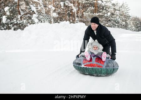 Fröhlicher Vater reitet seine Tochter auf einem Schlitten im verschneiten Wald Stockfoto
