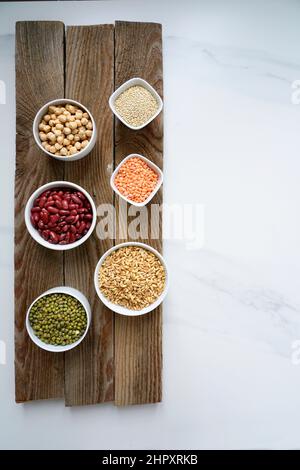 Vielfalt an ungekochten Superfood-Cerealien, Chia, roten Linsen, Perlmutt, roten Bohnen, Kichererbsen, grüne Azuki auf weißem Marmorboden, flaches Layout, vi Stockfoto