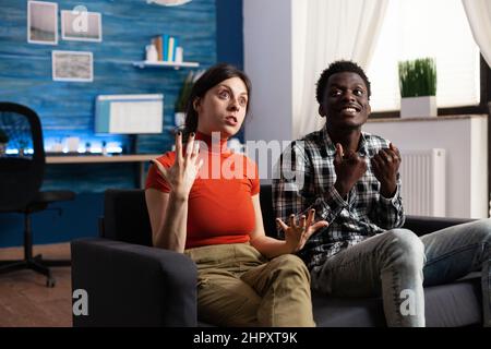 Zornige multirassische Personen, die auf ungesunde Konflikte reagieren, während sie agressiv gestikulieren. Erwachsene, die sich über Eheprobleme streiten, kämpfen zu Hause im Wohnzimmer auf der Couch Stockfoto