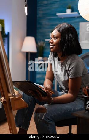 Designer Frau Student Browsing Zeichnen Sie Inspiration auf einem Tablet-Computer sitzen vor in Leinwand Zeichnung Skizze mit Bleistift im Kunstatelierin. Junge Künstlerin, die bei einem kunstauthischen Meisterwerk arbeitet Stockfoto