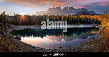 Carezza, Italien - Panoramablick auf den Karersee (Lago di Carezza) mit den italienischen Dolomiten, die sich auf dem See spiegeln. Warmer Herbstaufgang, aufgehende Sonne a Stockfoto