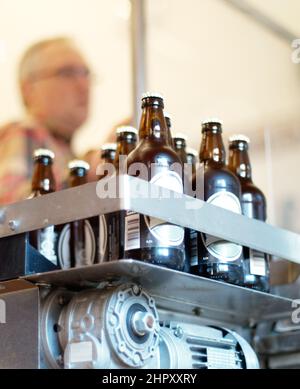 Ein köstliches neues Gebräu. Aufnahme einer Partie Flaschenbier in einer Brauerei mit einem Mitarbeiter im Hintergrund. Stockfoto