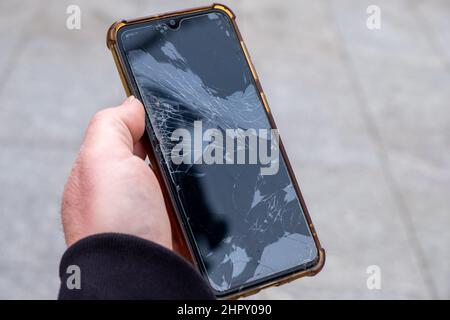 Ein Mann, der ein Telefon mit einem defekten Bildschirm hält Stockfoto