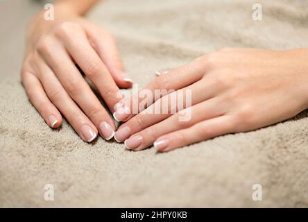 Crop Hände unkenntlich weiblich mit glatter Haut und stilvolle Französisch Maniküre auf weichen beigen Handtuch in hellen Salon nach Schönheitsverfahren Stockfoto