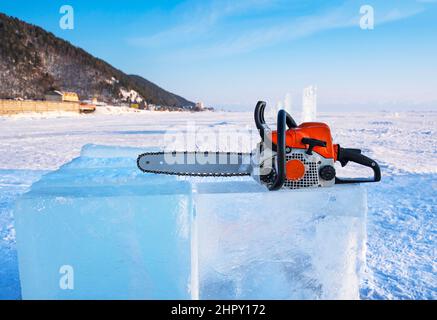 Die Benzinsäge liegt auf einem Eisblock für die Herstellung von Skulpturen am Baikalsee. Stockfoto