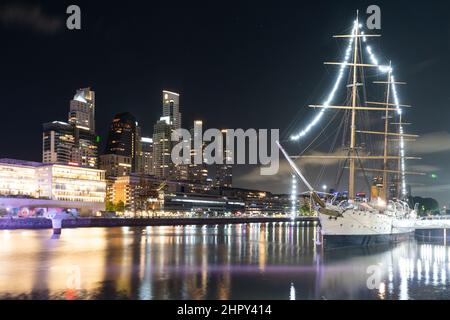 Nachtaufnahme des alten Bootes am Hafen, mit den Stadtlichtern in Puerto Madero, Buenos Aires, Argentinien. Stockfoto