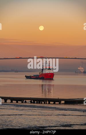 Morgendämmerung und Moonset über der Dartford-Brücke an einem kalten Wintermorgen mit Schlepper im Vordergrund Stockfoto