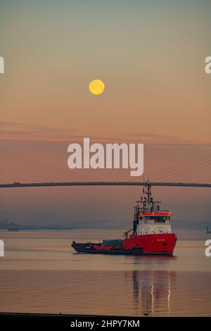 Morgendämmerung und Moonset über der Dartford-Brücke an einem kalten Wintermorgen mit Schlepper im Vordergrund Stockfoto