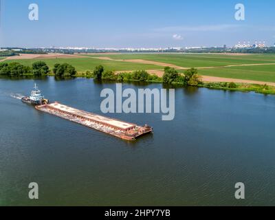 Kleines Schleppboot schiebt Barge entlang ruhigem Wasser vorbei an Feldern Stockfoto