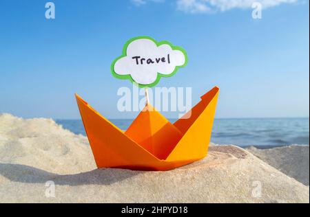 Orange kleines Papierboot auf Sandy Seashore auf dem Hintergrund Meer und sauberer blauer Himmel Nahaufnahme am sonnigen Sommertag. Halten Sie sich an den weißen grünen leeren Sprechbubl Stockfoto