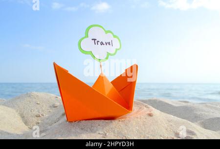 Orange kleines Papierboot auf Sandy Seashore auf dem Hintergrund Meer und sauberer blauer Himmel Nahaufnahme am sonnigen Sommertag. Halten Sie sich an den weißen grünen leeren Sprechbubl Stockfoto
