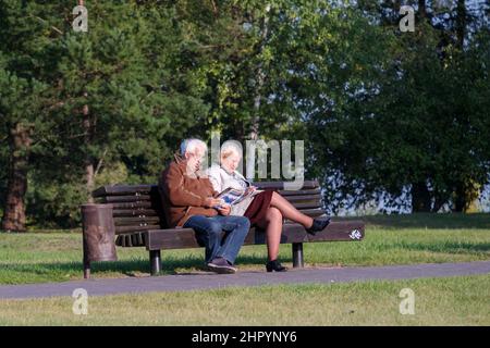 Senioren, ältere Paare im Park auf einer Bank, die Zeitschriften lesen und ein Kreuzworträtsel lösen Stockfoto