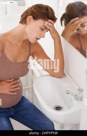 Ich fühle mich so krank. Eine Schwangerin, die im Badezimmer mit Morgenkrankheit zu kämpfen hat. Stockfoto