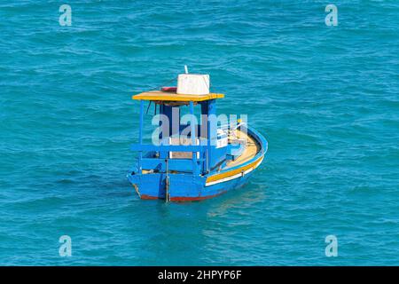 Kleines blaues und gelbes Boot, verloren und leer mitten im Meer, nur von Wasser umgeben. Stockfoto