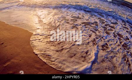 Meereswelle mit weißem Schaum rollt über das sandige Ufer des Strandes. Draufsicht. Stockfoto