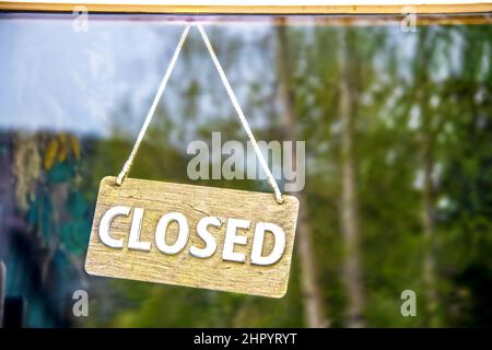 Rustikales, geschlossenes Holzschild an einem Seil, das an der Business-Glastür hängt und Kiefernwald reflektiert - Nahaufnahme und Platz für Kopien Stockfoto