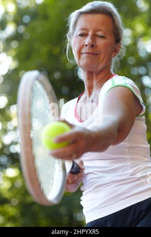 Den Ball im Auge behalten. Ältere Frau, die sich zum Dienst bereit gemacht hat - Tennis. Stockfoto