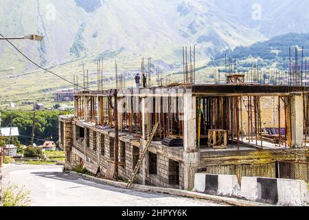 2019 07 18 Stepantsminda Georgia - mehrstöckiges Betonblockgebäude mit vielen Balken- und Betonblöcken und zwei unkenntlichen Männern Stockfoto