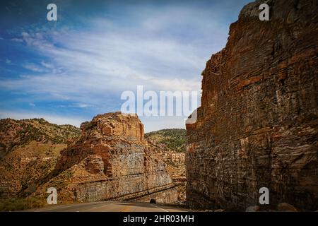 Highway Schnitt durch einen soliden Felsberg in den nördlichen Utah USA Badlands - Fahrzeuge fahren steil bergab und die Sonne spiegelt sich auf dem steilen Schnitt und auf der anderen Seite wider Stockfoto