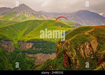 Roter Fallschirm gleitet über die Berge und wilden Schluchten des unteren Kaukasus in Georgien Stockfoto