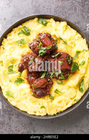 Typisches Gericht der brasilianischen Küche Rabada Oxtail mit Maisbrei Nahaufnahme auf dem Teller auf dem Betontisch. Vertikale Draufsicht von oben Stockfoto