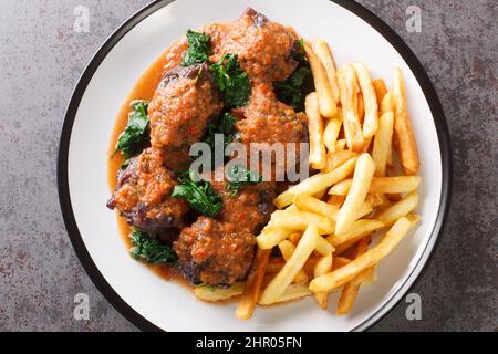 Ochsenschwanz in Sauce Rabo de toro serviert mit pommes auf weißem Teller auf dem Betontisch. Spanisches Gericht. Horizontale Draufsicht von oben Stockfoto