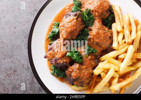 Fleisch für den Bulltail-Eintopf Rabo de toro serviert mit pommes auf weißem Teller auf dem Betontisch. Horizontale Draufsicht von oben Stockfoto