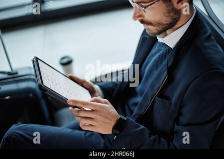 Geschäftsmann arbeitet auf einem digitalen Tablet, während er auf seinen Flug wartet. Nahaufnahme. Stockfoto