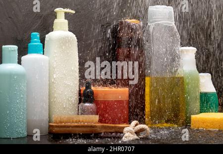 Nahaufnahme von Kosmetikprodukten in der Dusche mit Wasserspritzern auf schwarzer Keramik Stockfoto