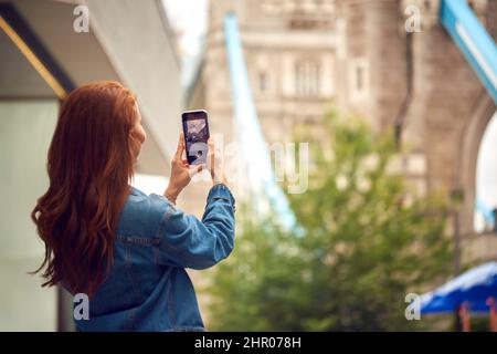 Vloggerin Oder Social Influencer In London, Die Fotos Auf Dem Mobiltelefon Der Tower Bridge Gemacht Hat Stockfoto