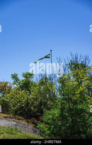 Die schwedische Flagge fliegt im Wind auf dem Fahnenmast hinter einem Busch. Stockfoto