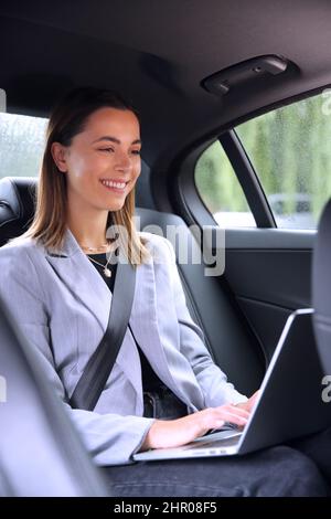 Geschäftsfrau, Die Auf Dem Rücksitz Eines Taxis Oder Autos Sitzt Und Am Laptop Arbeitet Stockfoto