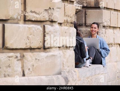 Zwei Studentinnen Der Universität Oder Der Hochschule Sitzen In Der Stadt Gegen Die Mauer Und Arbeiten An Einem Digitalen Tablet Stockfoto