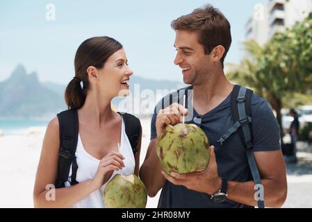 Wir hatten eine tolle Zeit im Paradies. Das junge Paar genießt einen Drink von einer Kokosnuss, während es einen Tag am Strand genießt. Stockfoto