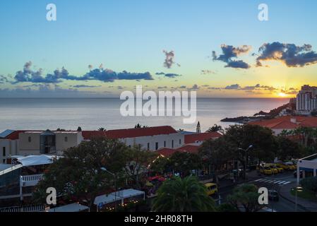 Ein Teil der Stadt Funchal im Vordergrund und der Sonnenuntergang über dem Meer im Hintergrund, Bild von Funchal Madeira, Portugal. Stockfoto