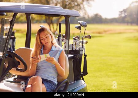 Frau, Die Im Buggy Sitzt, Auf Dem Golf Eine Runde Spielt Und Die Punktekarte Überprüft Stockfoto