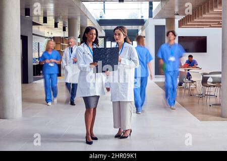 Zwei Ärztinnen In Weißen Mäntel Diskutieren Über Patienten-Scans Im Stark Frequentierten Krankenhaus Stockfoto