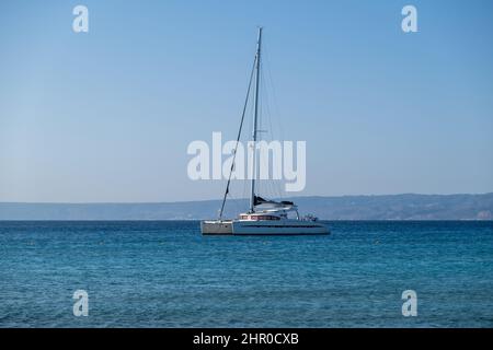Segelboot-Katamaran vor Anker am wellpled Sea, Land und blauen Himmel Hintergrund. Sommerurlaub Stockfoto